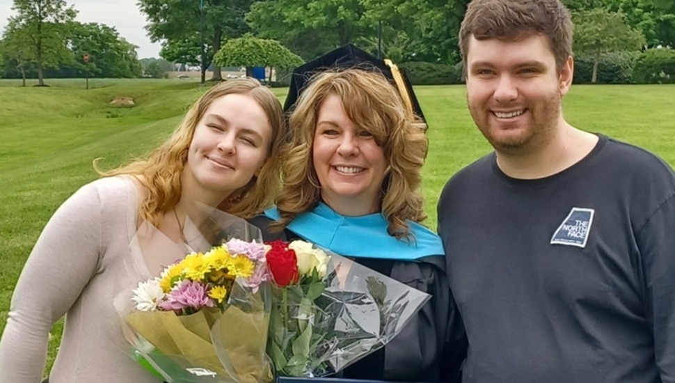 College graduate in cap and gown poses for a picture with her kids.