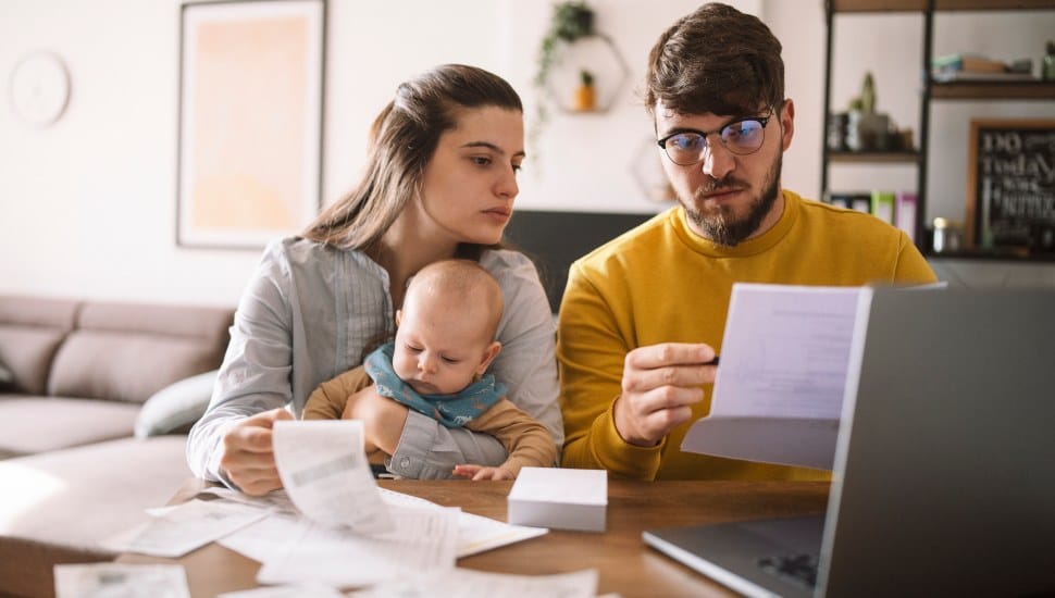 Worried couple with new baby looking at bills at kitchen table.