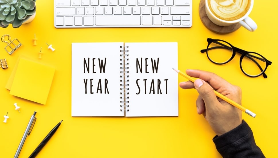 Person writing in notebook that says new year and new start.