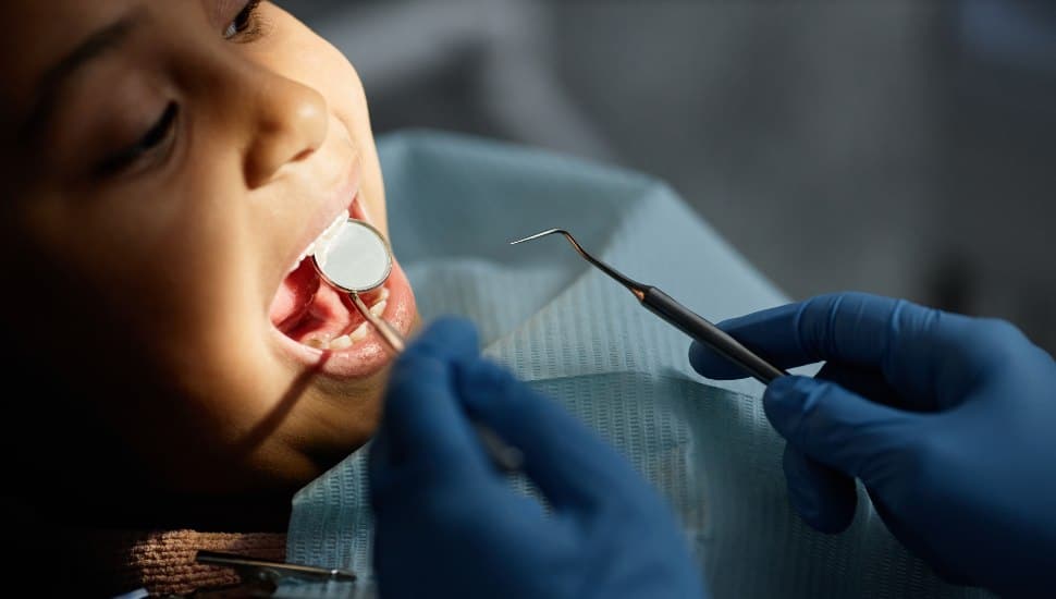Closeup of little child in teeth checkup at dental clinic, unrecognizable dentist holding tools and mirror.