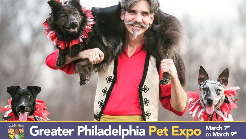 A performer dressed in a red and beige circus-style outfit with a mustache and a fur stole poses with three dogs wearing red and white ruffled collars. One dog is perched on his shoulders, while the other two stand beside him. The image promotes the Greater Philadelphia Pet Expo, taking place from March 7th to March 9th.