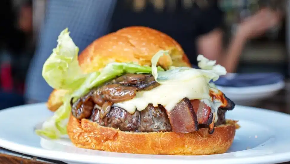 A burger with onions, mushrooms, cheese, house made bacon, on a potato bun.