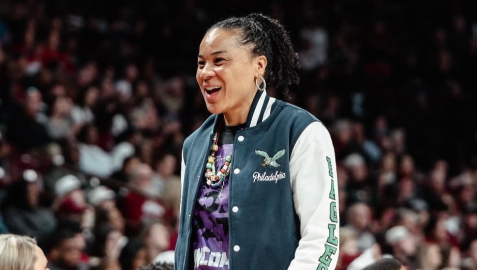 Dawn Staley during a game, smiling and wearing an Eagles jacket.