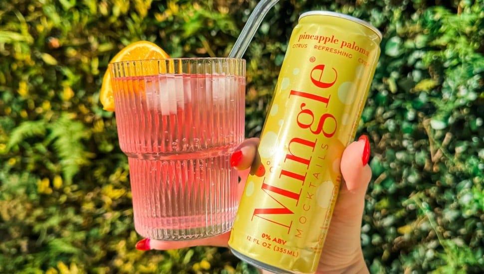 Woman's hand holding a Mingle Mocktails can and a glass.
