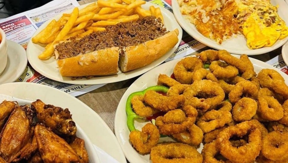 A cheesesteak with fries, onion rings, wings, and an omelet.