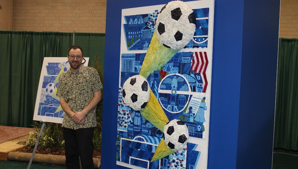 Nicholas McClinton poses next to floral interpretation of his designed poster.