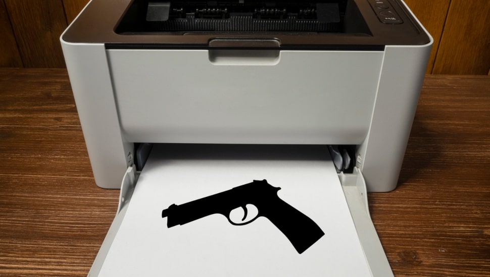 An image of gun printed out on paper coming out of a printer.