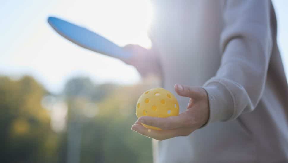 Pickleball athlete serving a ball with a racket.