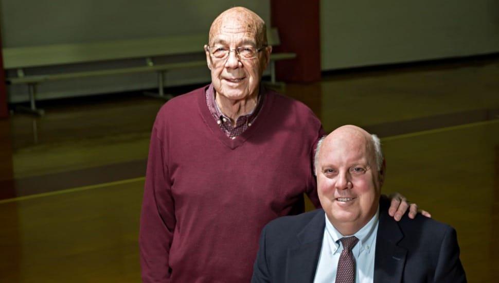 Father and son pose for a photo inside a basketball gym.