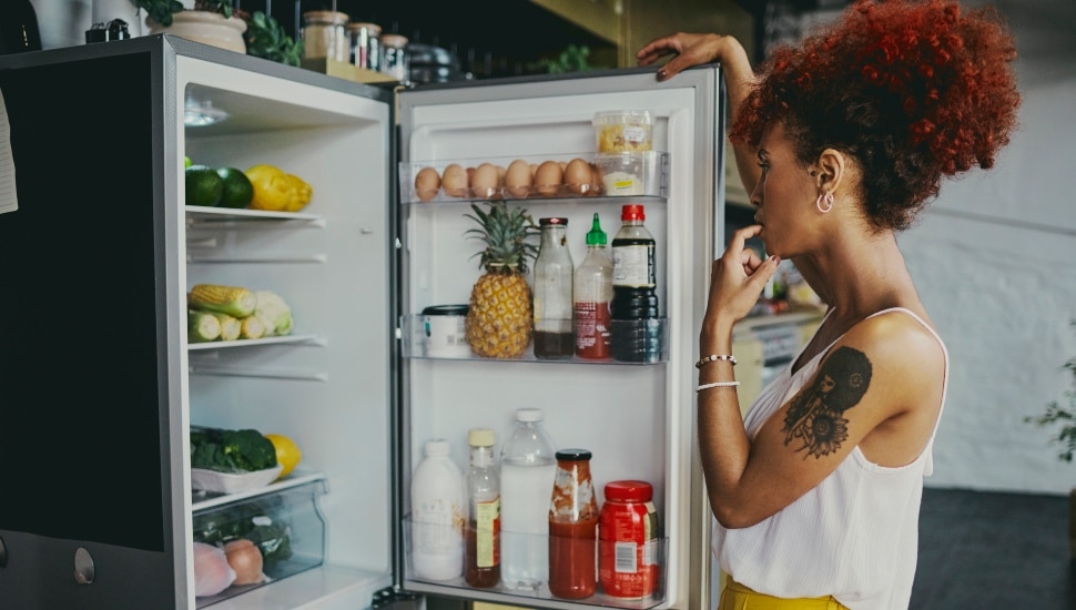 A woman looking into a fridge with fruits and vegetables inside.