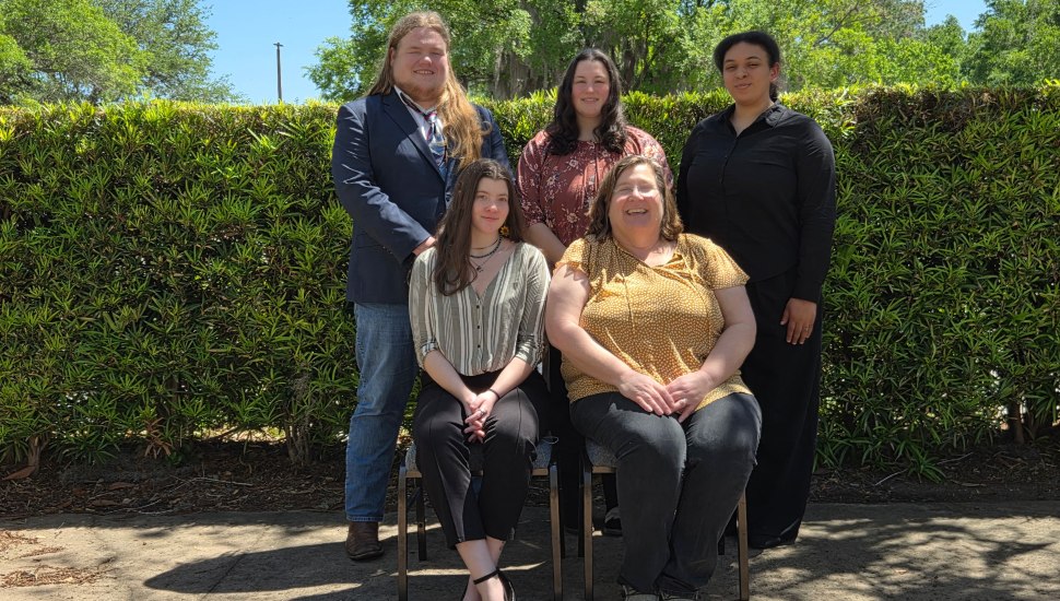 Five college students pose for a group photo in front of bushes.