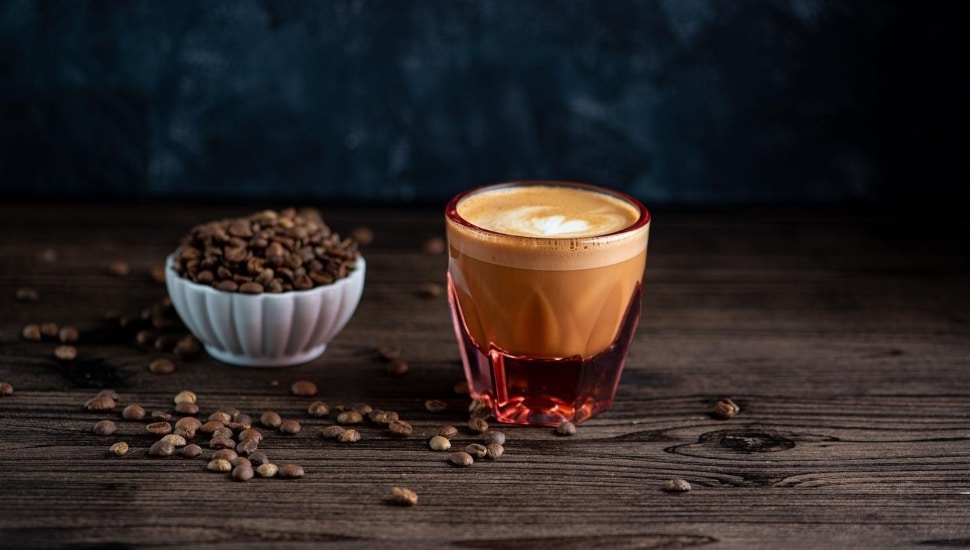 A cup of coffee with coffee beans next to it.