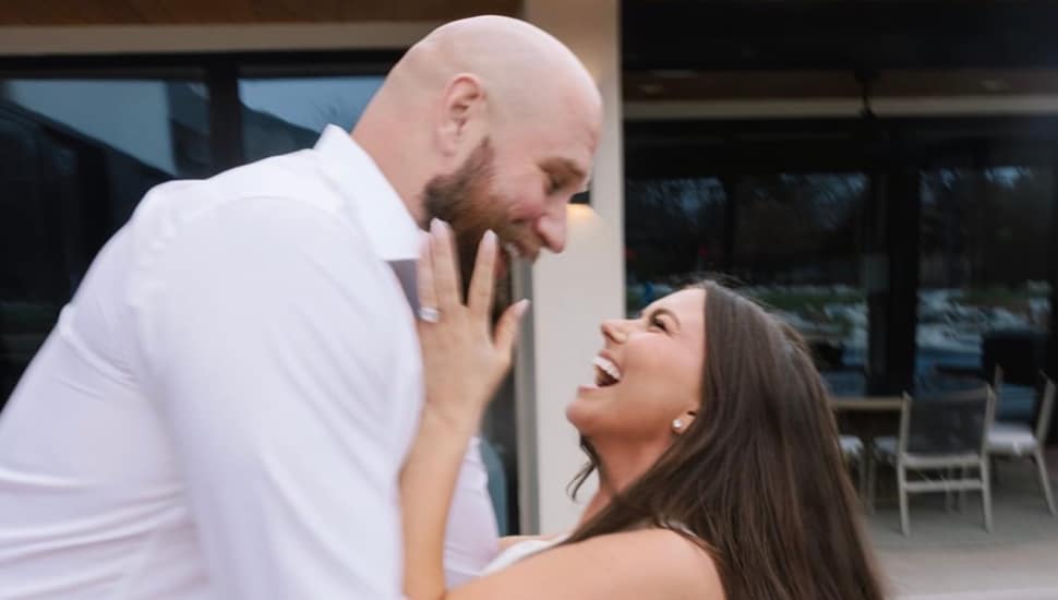 Lane Johnson holding his new new fiancée Kelsey Holmer around the waist, while she grabs his face smiling.