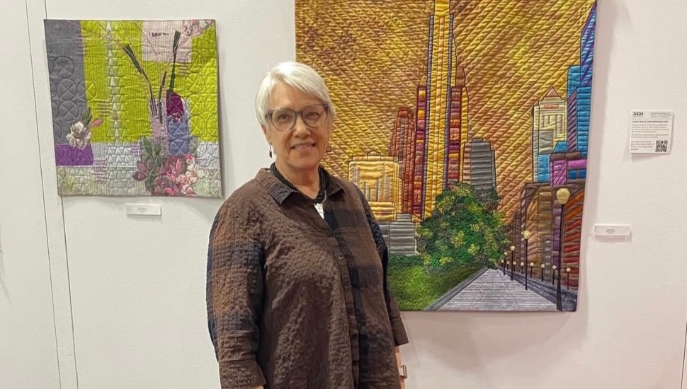 Rachel Blosser Derstine standing alongside her "JFK Boulevard" quilt a craft show.
