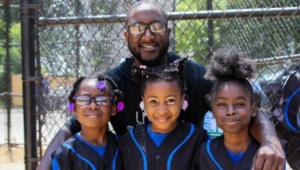 Haneef Hill in the background, on the softball field, with three young people.
