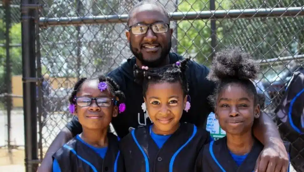 Haneef Hill in the background, on the softball field, with three young people.
