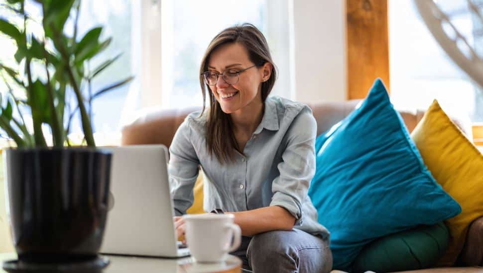 A woman sitting in her living room with her laptop and coffee.