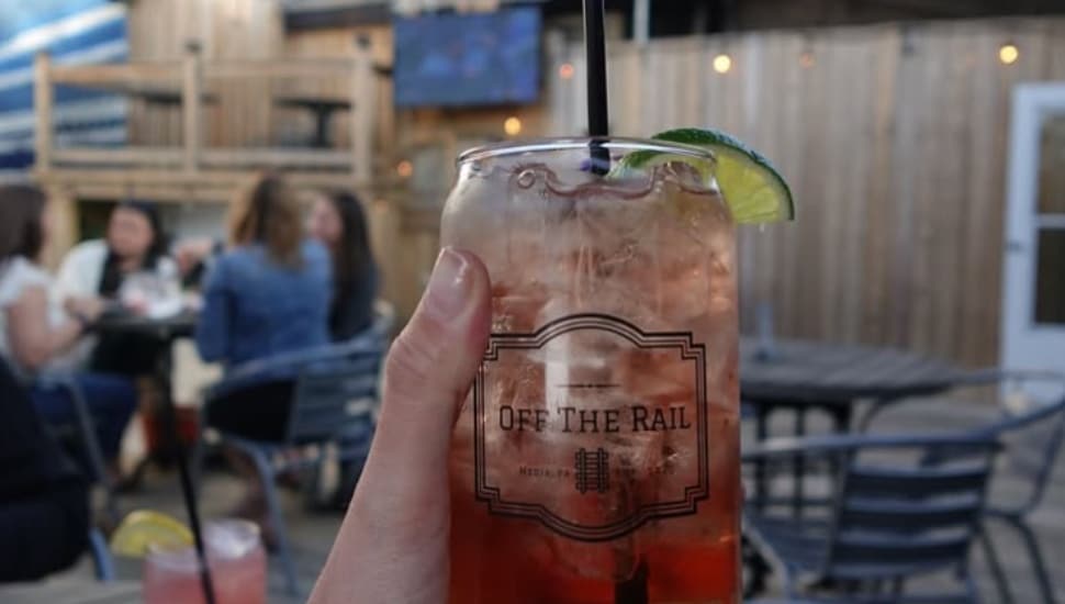 A hand holds a glass with a special cocktail while at the rooftop bar at Off the Rail in Media Borough.