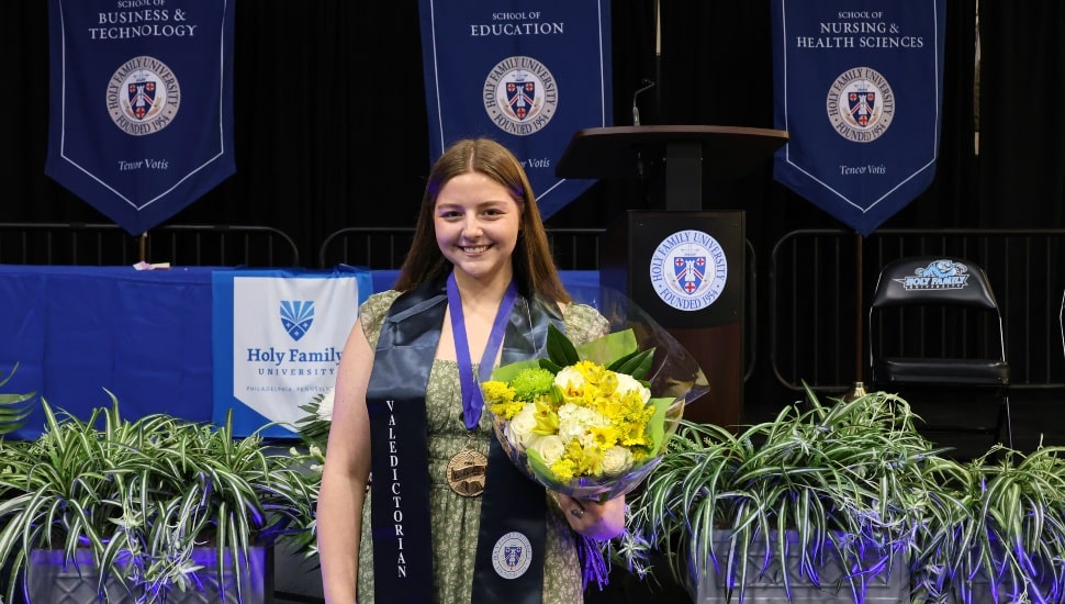 Female college valedictorian smiles and holds yellow flowers.