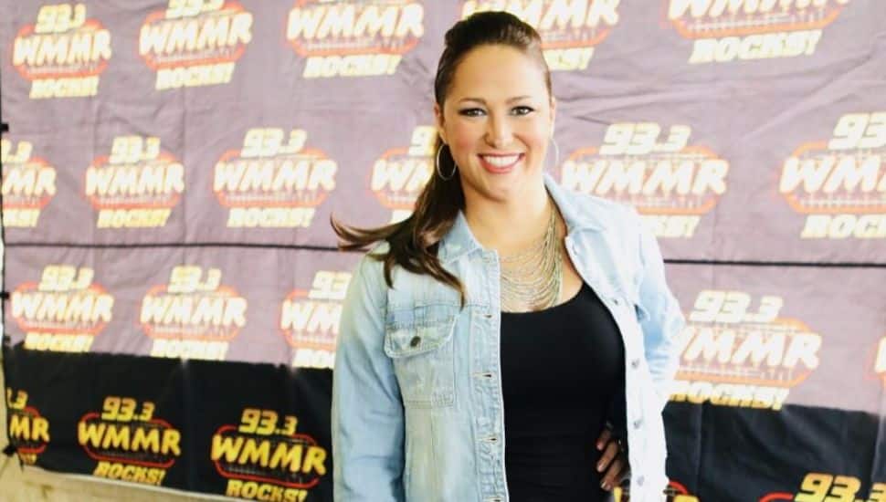 Kathy Romano poses in a jean jacket in front of a WMMR backdrop.