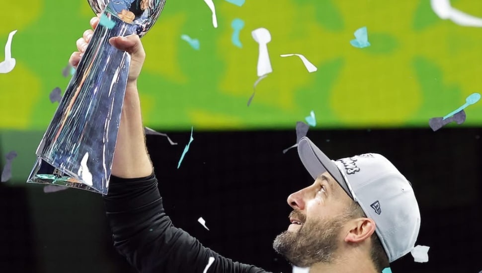 Nick Sirianni smiling and holding the Lombardi trophy in the air with confetti in the background.