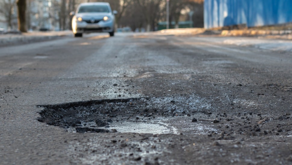 A pothole in the road and a car in the background that is moving towards this pothole.