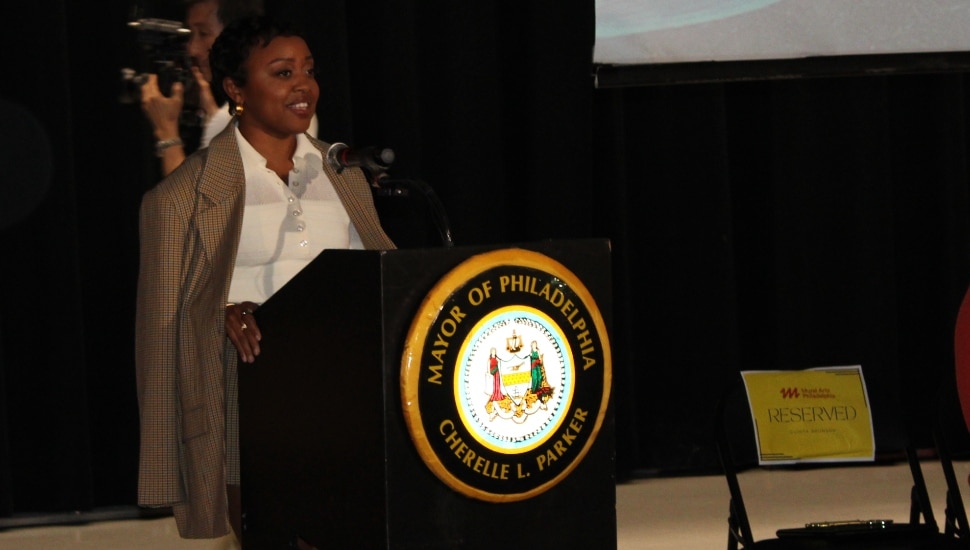 Quinta Brunson speaking at podium inside the auditorium at Andrew Hamilton School.