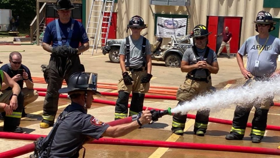 A firefighter using a hose with other firefighters in the background.