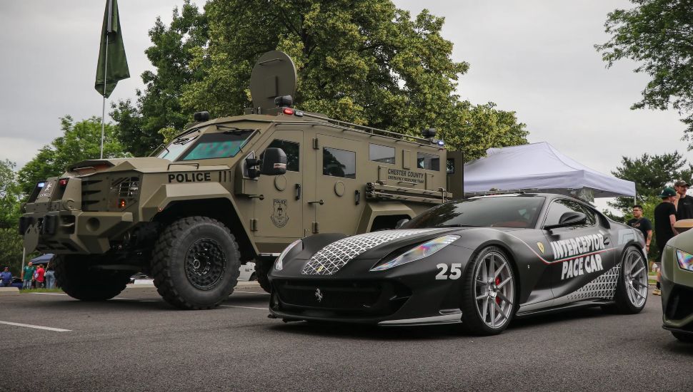 A military vehicle is parked next to a sports luxury car.
