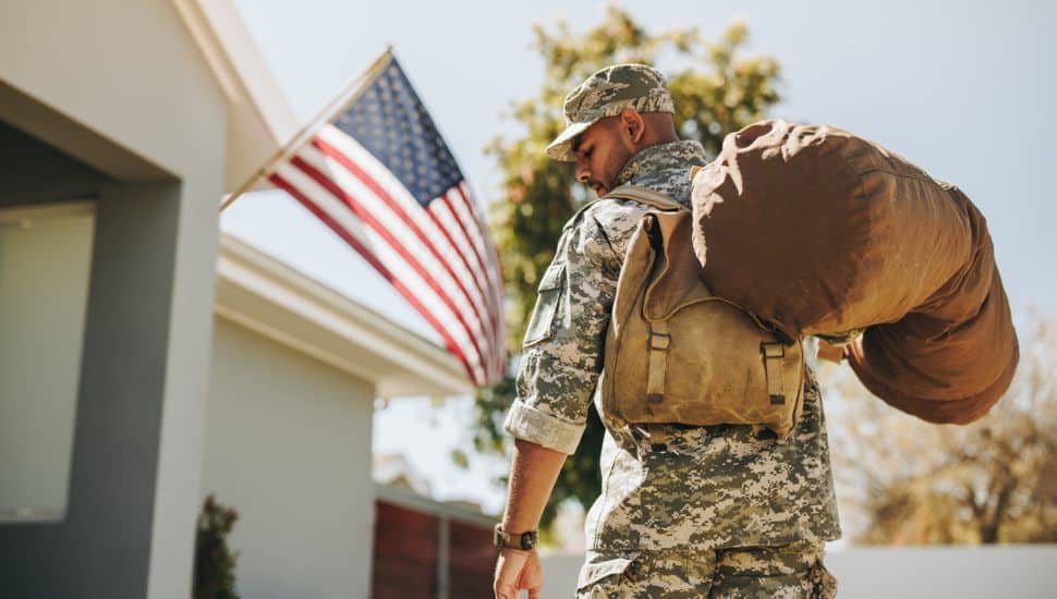 Rearview of a patriotic young soldier walking towards his house with his luggage. Courageous American serviceman coming back home after serving in the military.