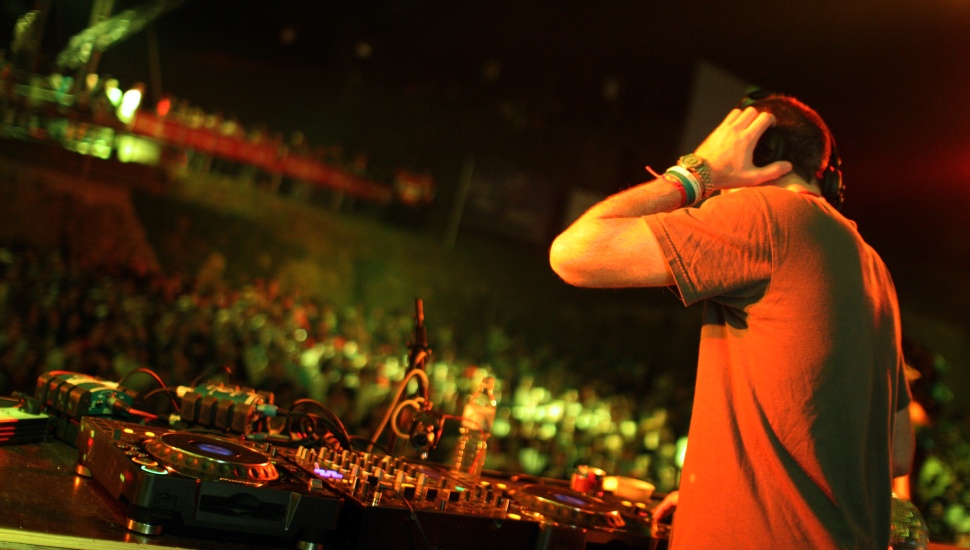 A DJ playing inside a venue with a crowd.
