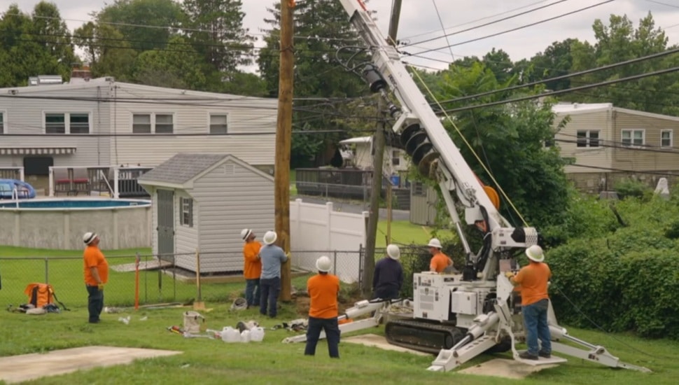 Utility workers raise a utility pole in a residential backyard.