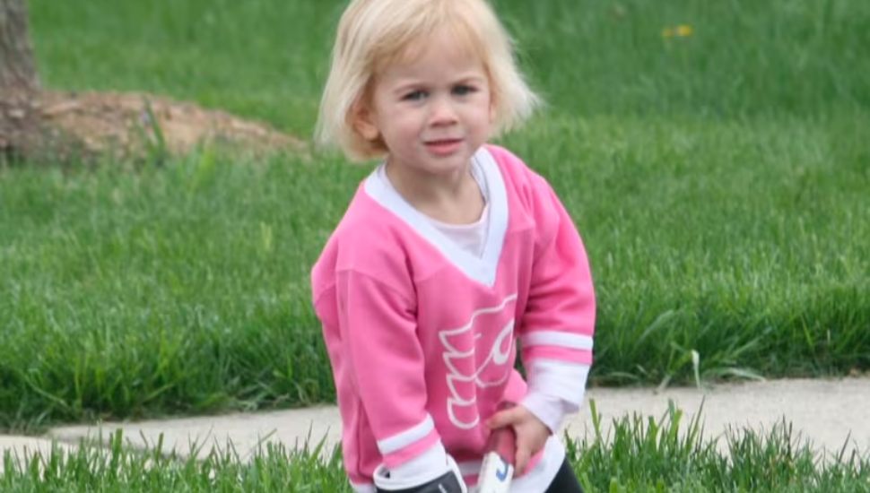 Young Sloane Hartmetz with pink Flyers shirt and tiny hockey stick.