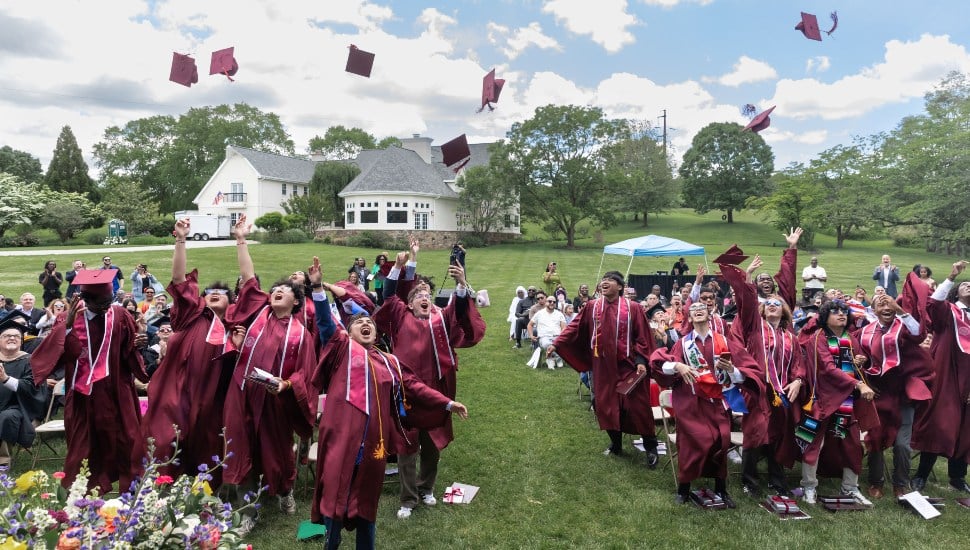 High school graduates in maroon caps and gowns toss their caps in the air.