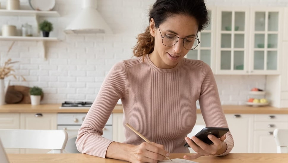 Woman calculates savings while seated at her kitchen table.