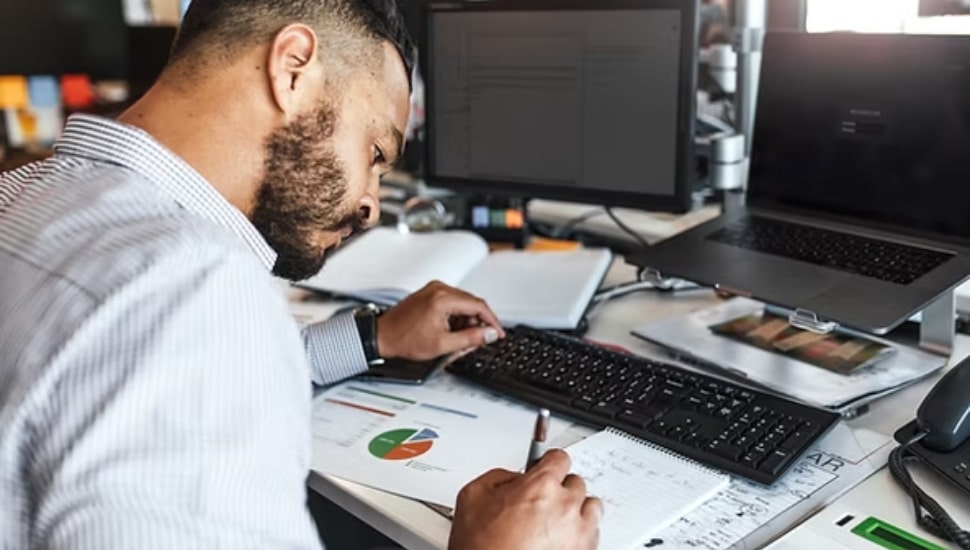 A team member completing cybersecurity work on a computer and notepad.