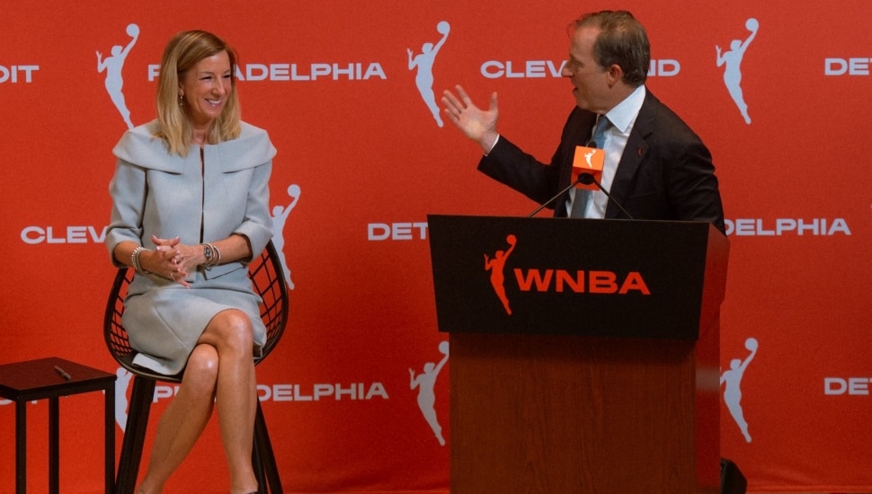 Josh Harris at the podium looking to his right at Cathy Engelbert during a press conference.