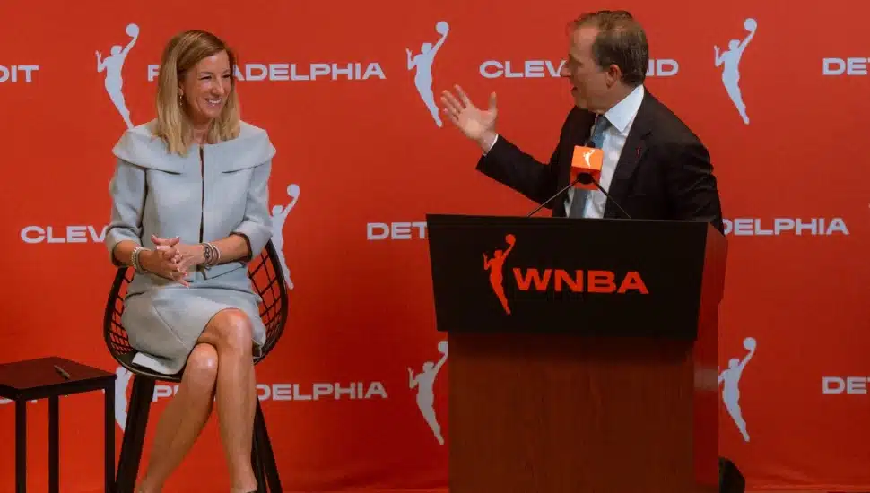 Josh Harris at the podium looking to his right at Cathy Engelbert during a press conference.