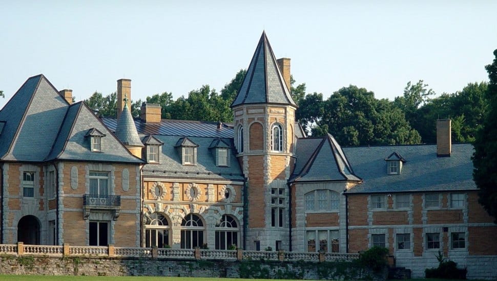 Exterior view of Cairnwood Estate, a grand Gilded Age mansion with turrets, arched windows, and intricate stonework, surrounded by trees.