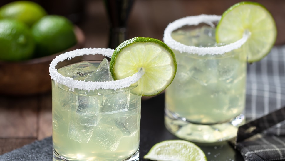 Margarita cocktail with ice, lime slice and salt rim on a black slate board.