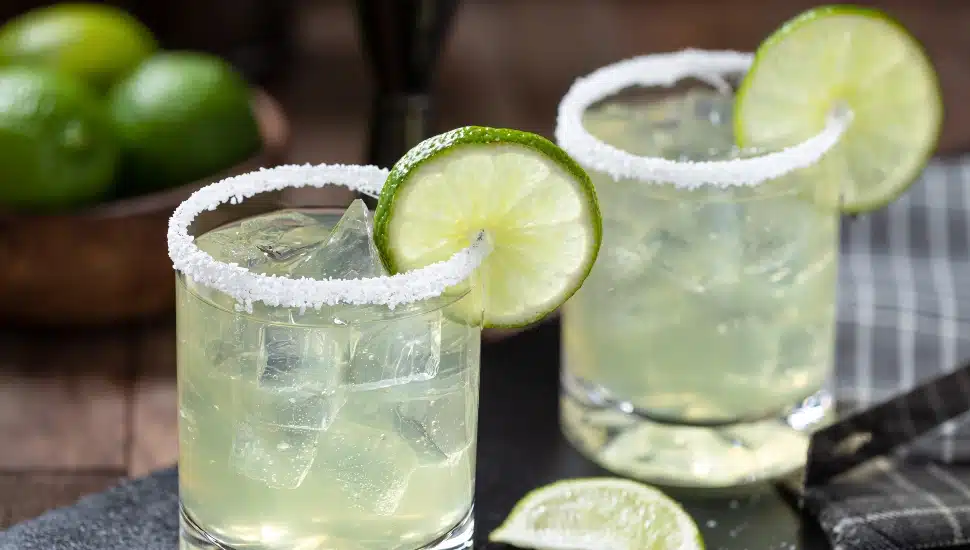 Margarita cocktail with ice, lime slice and salt rim on a black slate board.