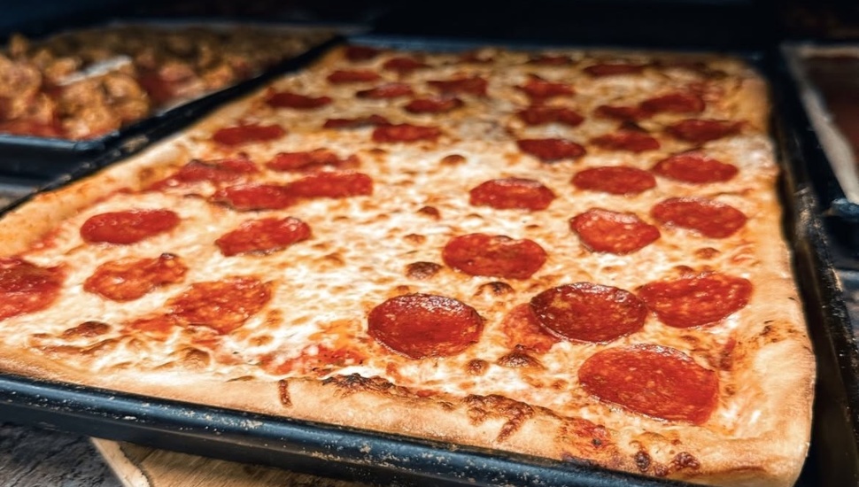 A square pepperoni and cheese pizza being taken out of an oven.