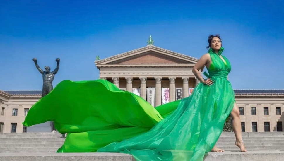 A woman wearing a long, green dress in front of the Philadelphia Museum of Art and Rocky statue.