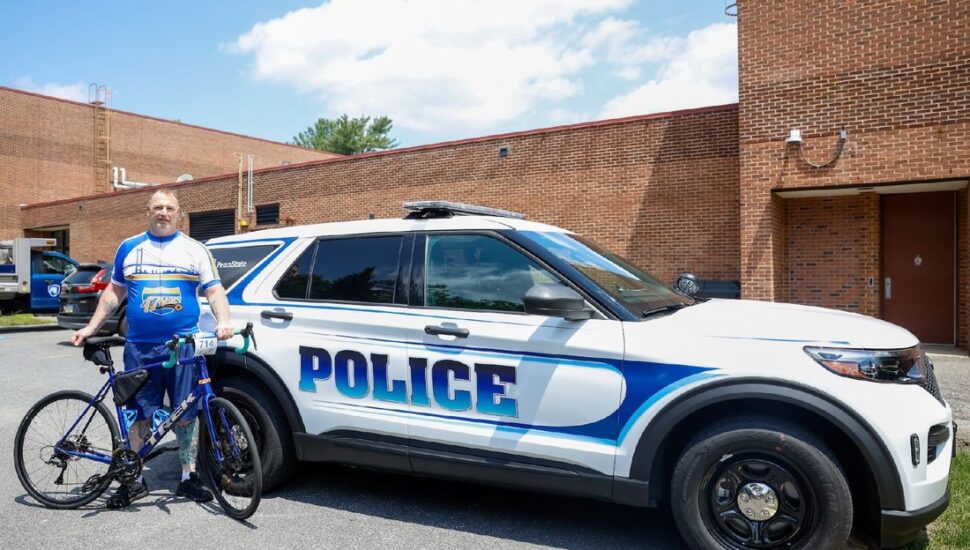 Bill Carter a Penn State Brandywine University Police and Safety Officer stands with his bike in front of a police car.