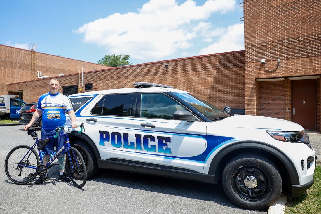 Bill Carter a Penn State Brandywine University Police and Safety Officer stands with his bike in front of a police car.