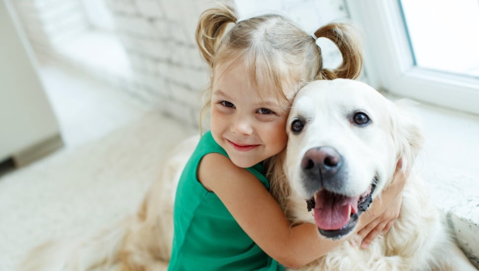 A young girl smiling and hugging her pet dog.