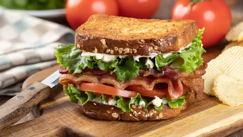 Blt sandwich made with bacon, lettuce and tomato on toasted whole grain bread on a wooden cutting board.