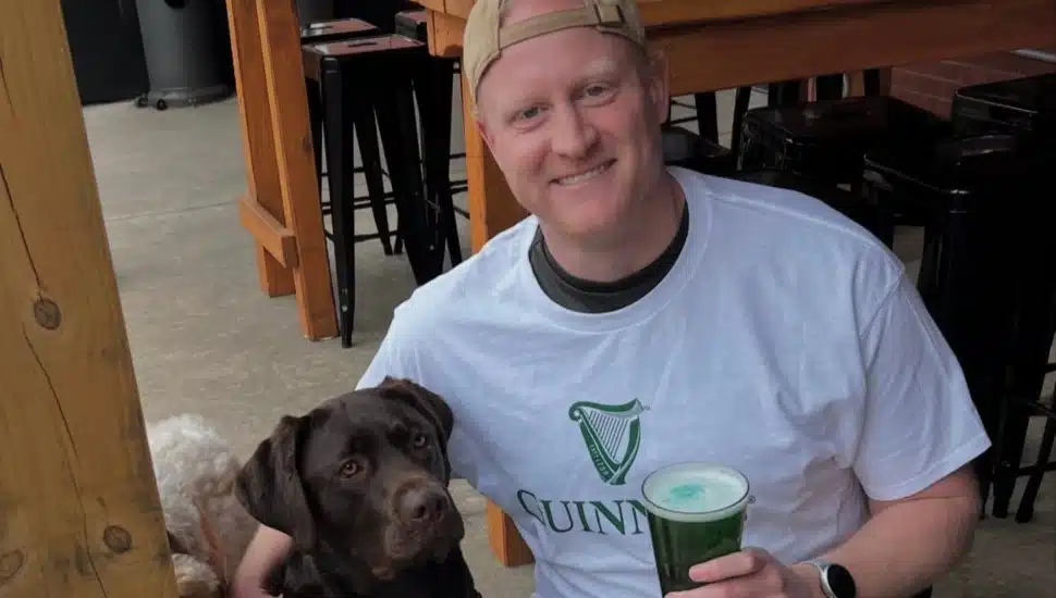 A man holding a beer with other arm around his dog.