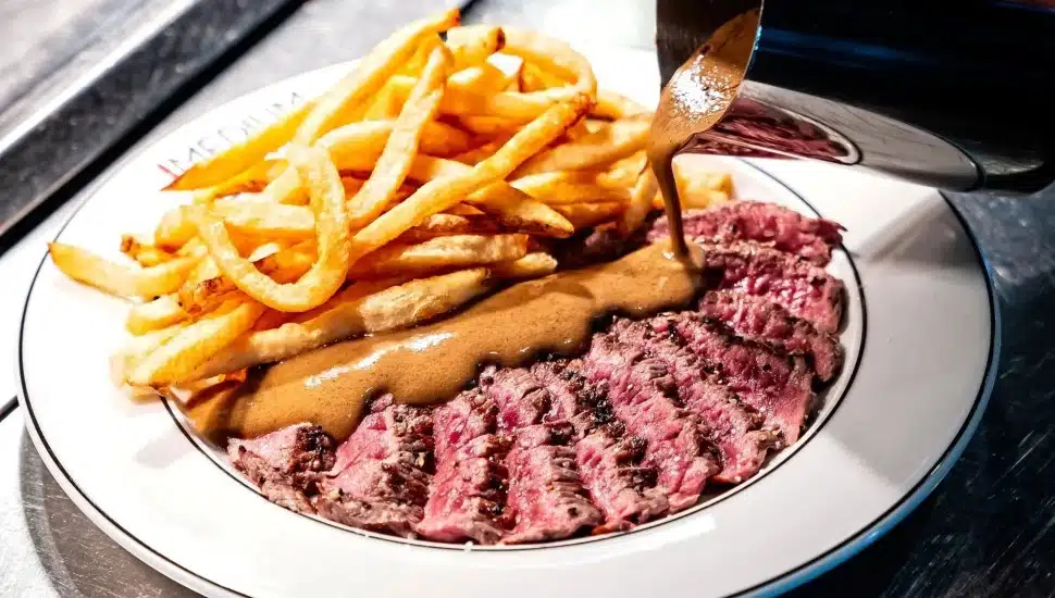 Steak frites with fries, and secret sauce being poured onto the steak.