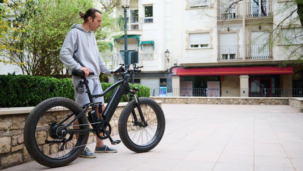Young Caucasian man in sports wear, renting and riding e-bike in the city.